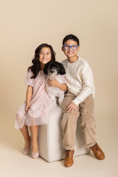 two kids posing with their dog in a chicago studio on a cream backdrop