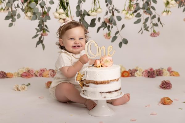 one year old girl smiling during a custom floral cake smash