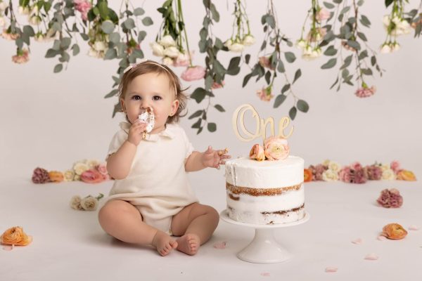 one year old girl eating cake during a floral garden cake smash session