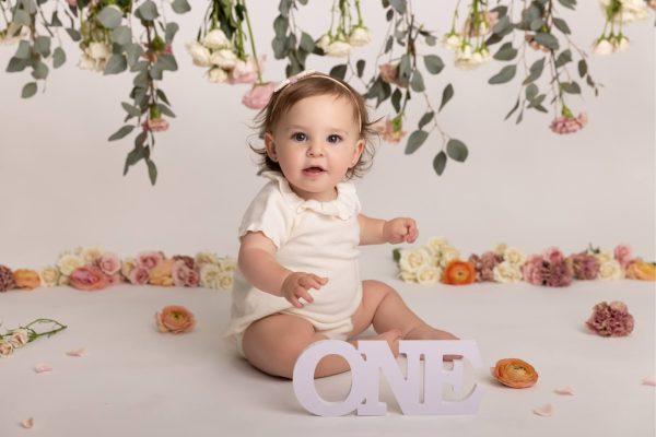 one year old girl smiling during a floral cake smash Chicago studio portrait session