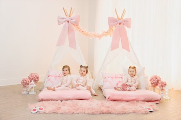 three one year old girls sitting on beds in a pink tent first birthday session