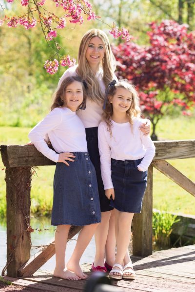 mom and daughters posing int he spring time on a bridge in a park