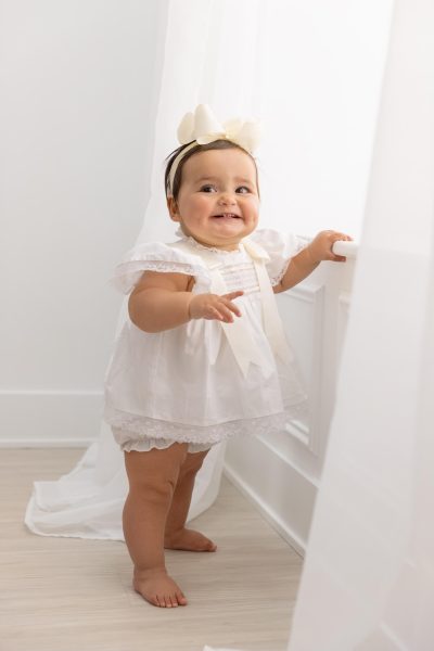 one year old girl in white smiling at white window in Chicago studio