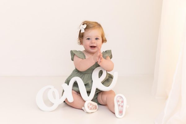one year old girl smiling and holding one sign