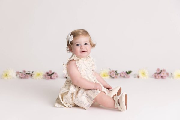 one year old girl sitting and smiling at her floral cake smash