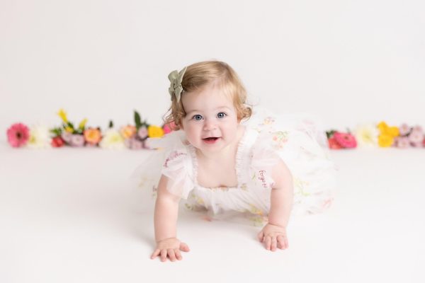 one year old girl crawling at her floral cake smash