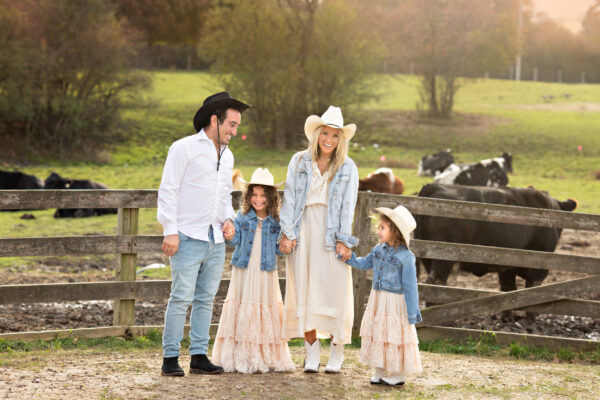 family posing on a farm with cows in the background