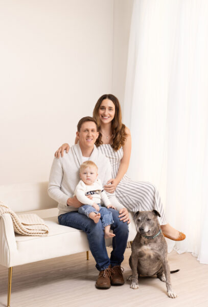 first birthday cake smash session family portrait sitting on couch with dog in natural light studio area
