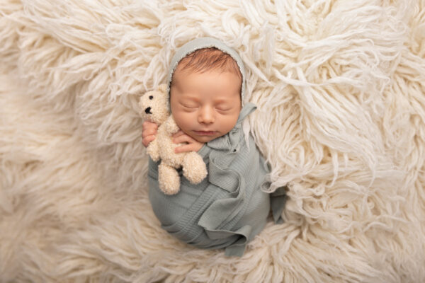 Sleeping newborn baby wrapped in sage green swaddle posed on a rug in Chicago studio